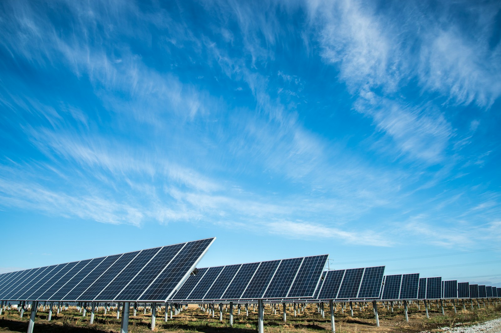 Filas de paneles solares azules sobre un terreno con pasto, bajo un cielo despejado con algunas nubes.